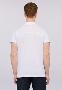 Bílá polokošile s krátkým rukávem a plochým límcem. Hladký bavlněný materiál, s jemným horizontálním švem na zádech.