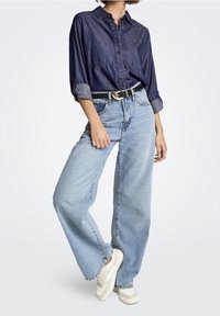Person wearing a dark blue denim shirt with rolled sleeves, light blue high-waisted wide-leg jeans, black belt, and white sneakers.
