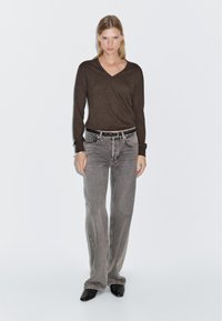 Brown long-sleeve top with a V-neck, paired with gray straight-leg jeans and black ankle boots. Model stands against a light background.