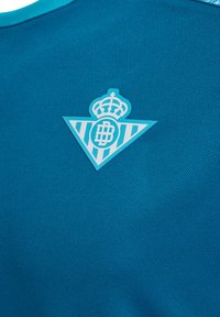 Turquoise stof heeft een gestructureerd patroon met een lichtblauw logo. Het logo bevat een kroon en een driehoekig ontwerp met strepen.