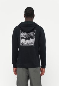 Felpa nera con cappuccio e grafica di montagna bianca sulla schiena. Presenta un cappuccio con coulisse e polsini a costine, realizzata in tessuto morbido.