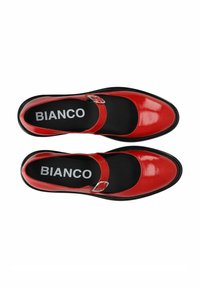 Zapatos Mary Jane de charol rojo con punta redonda y suela negra, que cuentan con una correa ajustable con hebilla y plantilla con marca.
