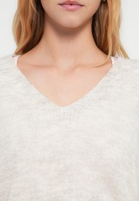 Camisola de decote em V cinza claro feita de tecido de malha macia. Apresenta acabamento texturizado e um corte descontraído com um brilho subtil.