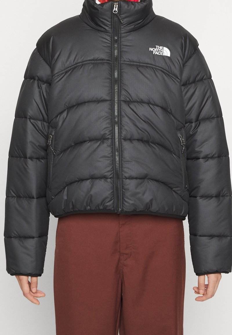 Czarna kurtka puchowa z poziomym pikowaniem, wysokim kołnierzem, zapięciem na zamek i bocznymi kieszeniami. Na piersi znajduje się logo The North Face.