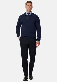 Námořnický pletený svetr s polo límečkem, přehozený přes světle modrou košili. V kombinaci s pruhovanými kalhotami a černými botami.