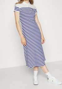 Paskowana sukienka midi w kolorze kremowym i niebieskim, z kołnierzykiem polo, krótkimi rękawami i dopasowanym krojem. Założona z białymi trampkami i skarpetkami.