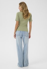 Top ribbed de culoare verde măsliniu cu mâneci scurte, asociat cu blugi largi, cu talie înaltă, de culoare albastru deschis. Design simplu, ajustat, dintr-un material texturat.
