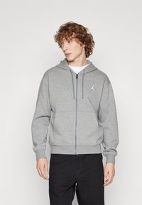 Grå zip-up hettegenser laget av mykt stoff, med kengurulomme, ribbestrikkede mansjetter, og en hvit logo på venstre bryst.