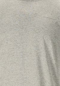 Tissu gris clair avec texte imprimé et logo subtils, à peine visibles, dans une teinte légèrement plus foncée.