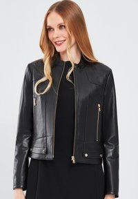 Zwarte leren jas met een slim fit, voorzien van gouden ritsen op de zijzakken en aan de voorkant. Gladde textuur en minimalistisch kraagontwerp.