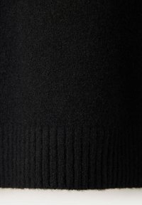 Gros plan sur un tissu tricoté noir avec un ourlet côtelé, montrant un matériau doux et texturé.