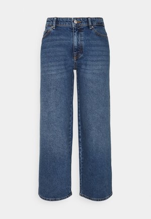 Jean bleu à jambes larges avec bouton et fermeture éclair à l'avant, passants de ceinture et coutures visibles sur un fond uni.