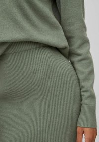 Ensemble tricoté comprenant un pull et une jupe dans une teinte d'olive atténuée. Présente une texture côtelée et des manches longues. Le tissu douillet tombe doucement.
