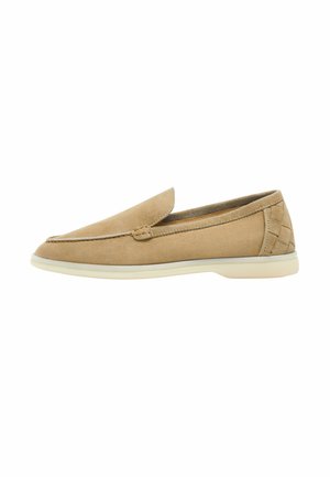 Mocassin beige en suède à enfiler, avec semelle en caoutchouc blanche et détails cousus au talon et sur le côté supérieur, vu de l'extérieur.