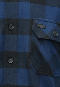 Camicia a quadri blu e nera realizzata in tessuto morbido, con bottoni neri e una tasca sul petto con logo Lacoste nero.