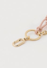 Kuldse metallist võtmehoidja, millel on ümarlõikeline rõngas ja väike karabiinilukk ning roosa nahast rihm, mis on ühes otsas sõlmega seotud.