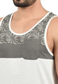Graues und weißes Trägertop mit Floral-Muster am Ausschnitt, zweifarbigen Farbkombinationen und einem kleinen Brusttaschen-Detail. Weicher Stoff.