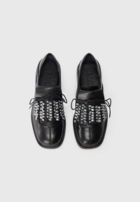 Black leather shoes with a textured design, featuring a covered toe and lace-up front adorned with silver studs across the vamp.