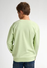 Lichtgroene sweatshirt met een ronde halslijn, lange mouwen en geribbelde manchetten. Zachte textuur en relaxte pasvorm, gedragen met blauwe jeans.