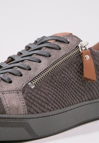 Grau strukturierten Leder Sneaker mit einem Reißverschlussdetail, flachen grauen Schnürsenkeln und einem braunen Lederelement. Verfügt über eine Gummisohle für besseren Grip.