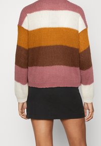 Maglione a maglie spesse nei colori rosa, bianco, senape e marrone a righe. Presenta polsini e orlo a coste. Abbinato a una mini gonna nera.