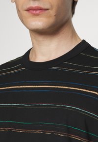 Nära bild av en person som bär en svart skjorta med flerfärgade horisontella ränder, som visar halsen och nedre delen av ansiktet.