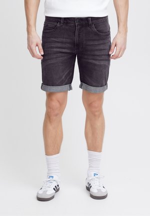 Sorte denimshorts med op rullede kanter, der har frontlommer og knapgylp, kombineret med hvide sokker og sorte, grå og blå sneakers.