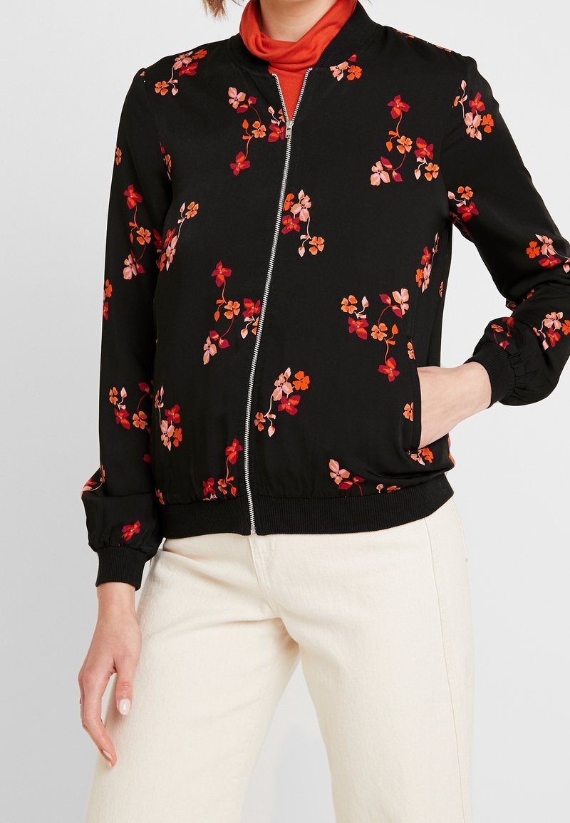 Giacca bomber nera con motivi floreali in rosso e rosa. Presenta una chiusura con zip frontale, polsini e vita a costine, realizzata in un materiale liscio e leggero.