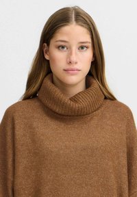 Pull à col roulé marron, côtelé, avec une coupe décontractée, présentant une texture douce et des manches amples. Design uni sans motifs ni accents.