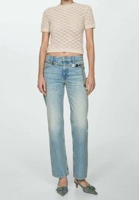 Lichtroze gebreide crop top met korte mouwen; blauwe rechte jeans met kettingaccent; model draagt grijze hakken met strikken.