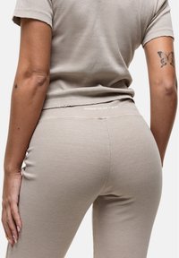 Beige geribbelde top met korte mouwen, met bijpassende legging, zichtbaar in een getailleerd ontwerp en textuurstof. Bevat een logo op de tailleband.