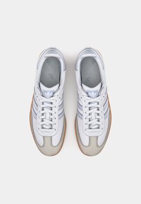 Vita och grå atletiska skor med tre blå ränder, texturerat läderövre, gummisula och en klassisk design. Har logotyp på tungan.