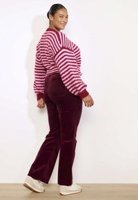 Suéter a rayas en rosa y rojo con mangas largas, combinado con pantalones de terciopelo burdeos y zapatillas blancas. Texturas suaves y diseño ajustado.