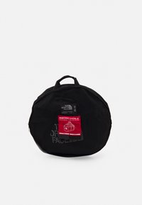 Sac de sport en mesh noir de forme circulaire, doté d'une étiquette rouge, de deux poignées et d'une fermeture zip. Dimensions : 37L x 12H x 14W cm.