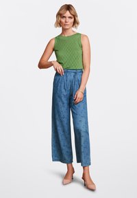 Grön ärmlös stickad topp med texturerade mönster, matchad med vida ljusblå byxor med en subtil abstrakt tryck och knytliv.