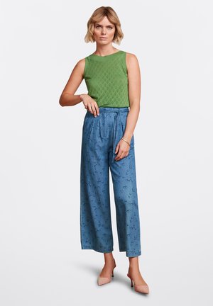 Groene mouwloze gebreide top met textuurpatronen, gecombineerd met lichtblauwe wijde broek met een subtiele abstracte print en een gestrikte taille.