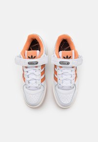 White leather sneakers with orange stripes, textured strap, round toe, perforations on the vamp, and cushioned interior.