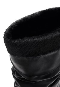 Bota de cuero negro con un suave puño de pelo sintético negro en la parte superior, con una textura lisa y un diseño recogido.