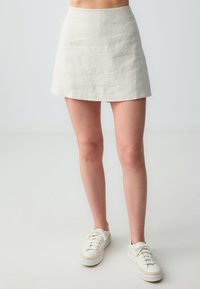 Jupe mini en lin blanc cassé, avec une taille ajustée et une coupe évasée. Associée à des baskets blanches avec une semelle texturée et des lacets.