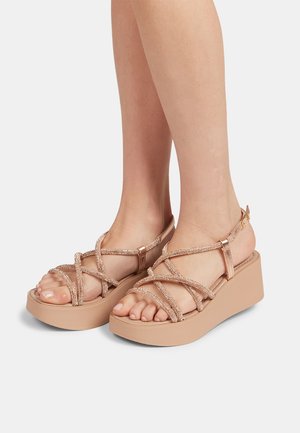 Rose gold platform sandals with crisscross straps, textured accents, and adjustable buckle. Solid rubber sole for stability and comfort.