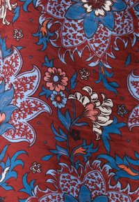 Tessuto rosso con intricate fantasie floreali in blu, rosa e bianco. Include forme di foglie dettagliate e accenti decorativi.