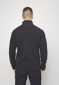 Schwarze Fleecejacke mit hohem Kragen, langen Ärmeln und flachen Nähten; weiche Textur und minimalistisches Design ohne sichtbare Logos.