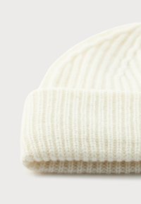 Zachte, crèmekleurige gebreide beanie met ribbelstructuur en omgeslagen rand, geplaatst op een lichte achtergrond.