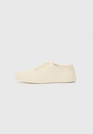 Zapatillas de lona marfil con perfil bajo, punta redondeada, diseño de cordones con seis ojales y suela de goma texturizada. Construcción minimalista y detalles acentuados.