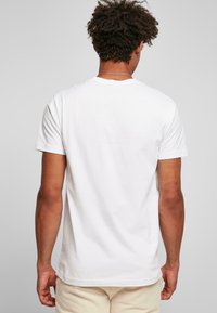 Tricou alb cu mânecă scurtă, văzut din spate, cu guler tip crew, textură moale din bumbac și croială lejeră. Detalii subtile de cusătură vizibile.