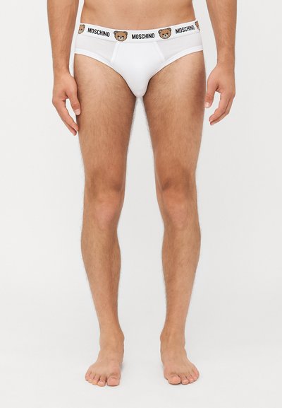 Weiße Herrenunterwäsche aus Baumwolle mit einem schwarzen Bund, der mit Moschino-Branding und einem Bärenlogo versehen ist. Glatte Textur und enganliegendes Design.