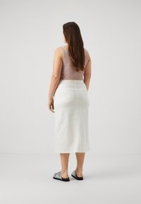 Falda de mezclilla blanca de longitud media, combinada con una camiseta sin mangas de rayas multicolores. Los zapatos son de color azul claro con detalles decorativos.