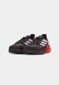 Zwarte hardloopschoenen met een gestructureerde mesh bovenkant, drie witte strepen en een rode verloop-midsol. Voorzien van een gevoerde kraag en rubberen buitenzool.
