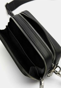 Borsa a tracolla in pelle nera con due scomparti con zip e una texture liscia. Presenta hardware in argento e una tracolla removibile.