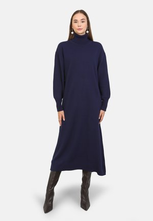 Robe col roulé marine en tissu doux, avec des manches longues et une coupe lâche, atteignant le milieu du mollet, associée à des bottes haute genoux.
